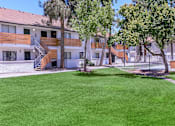 Thumbnail 18 of 28 - Spacious courtyard with lush green grass and trees in front of a white apartment building with wooden balconies at Tides on McDowell, AZ 85035