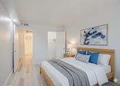 Thumbnail 6 of 20 - A bedroom with a bed, nightstand, and a painting on the wall.