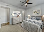 Thumbnail 5 of 19 - A bedroom with a large bed, a dresser, and a ceiling fan at Gilbert Square Apartments, Mesa, AZ