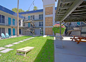 Thumbnail 17 of 19 - A patio with a table and chairs is surrounded by a grassy area and a building.