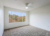 Thumbnail 9 of 21 - A room with a ceiling fan and a large window overlooking a desert landscape.