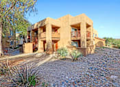 Thumbnail 20 of 21 - A building with a red balcony is surrounded by a gravel area and vegetation.
