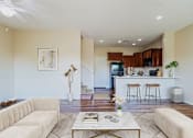 Thumbnail 1 of 29 - A living room with a white couch, a coffee table, and a kitchen area in the background.