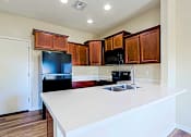Thumbnail 3 of 29 - A kitchen with a black fridge and microwave, brown cabinets, and a white countertop.