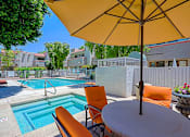 Thumbnail 58 of 94 - A yellow umbrella is over a table with chairs and a pool in the background.