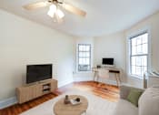 Thumbnail 6 of 21 - A living room with a television, a desk, and a couch.