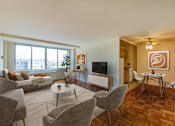 Thumbnail 8 of 47 - A living room with a grey couch, a white coffee table, and a brown rug.