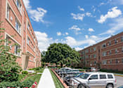 Thumbnail 15 of 23 - A sunny day at a brick apartment complex with cars parked on the street.