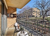 Thumbnail 8 of 43 - A balcony with a chair and table overlooking a tree and a building.