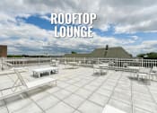 Thumbnail 31 of 37 - A rooftop lounge with white furniture and a blue sky in the background.
