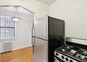 Thumbnail 9 of 21 - A black refrigerator and stove in a kitchen with a window and radiator.