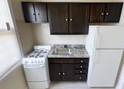 Thumbnail 5 of 16 - A kitchen with a white stove and refrigerator, and dark brown cabinets.