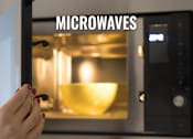 Thumbnail 25 of 26 - A person is holding a spoon in front of a microwave with a bowl inside.