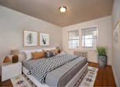 Thumbnail 7 of 17 - A bedroom with a bed, nightstand, framed pictures on the wall and hardwood floors at the strathmore apartments in downtown bethesda, md.