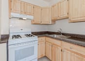 Thumbnail 12 of 29 - kitchen with wood cabinetry, gas range and tile flooring at parkside apartments in washington dc