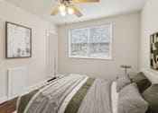 Thumbnail 6 of 17 - A bedroom with a bed, a ceiling fan, and a window with a view of trees outside.