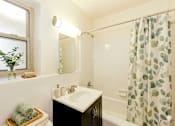 Thumbnail 7 of 24 - A bathroom with a white sink and a shower curtain with green leaves on it.