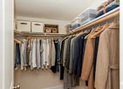 Thumbnail 7 of 20 - A white closet with clothes hanging and baskets on the shelf.