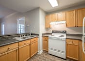 Thumbnail 25 of 35 - an empty kitchen with white appliances and wooden cabinets at Crogman School Lofts, Georgia