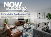 Thumbnail 1 of 30 - A living room with a sofa, chair, and coffee table with a sign that says "NOW Leasing" and "Refundable Application Fee".