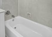 Thumbnail 32 of 34 - A white bathtub in a bathroom with a shower head and a square drain.