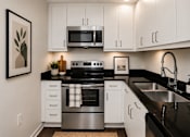 Thumbnail 18 of 34 - A modern kitchen with white cabinets and black countertops.