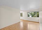 Thumbnail 39 of 50 - a living room with white walls and a window and wooden floors