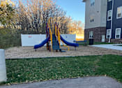 Thumbnail 108 of 115 - A playground with a slide and a bench in front of a building.
