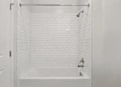 Thumbnail 10 of 25 - A white bathroom with a white tub and white tiles.
