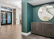 Thumbnail 18 of 23 - A hallway with a brown cabinet and a round mirror on the wall.