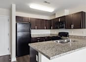 Thumbnail 18 of 33 - A kitchen with a black refrigerator and brown cabinets.