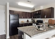 Thumbnail 7 of 33 - A kitchen with a black refrigerator and brown cabinets.