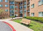 Thumbnail 52 of 75 - A brown bench is in front of a brick building.