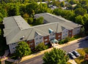 Thumbnail 1 of 21 - A large apartment complex with a green roof and a parking lot in front.