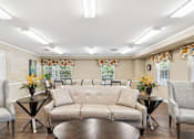 Thumbnail 6 of 14 - A living room with a beige sofa, two chairs, and two tables with vases of flowers.