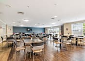 Thumbnail 4 of 14 - A large room with tables and chairs and a TV on the wall.