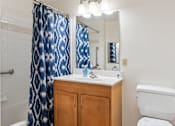 Thumbnail 13 of 21 - A bathroom with a white toilet, a sink with a wooden cabinet, and a blue shower curtain.