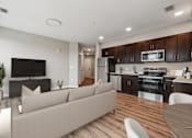 Thumbnail 2 of 17 - A modern living room with a couch, television, and kitchen area.