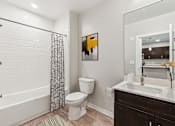 Thumbnail 6 of 17 - A bathroom with a white toilet, a shower with a black and white curtain, and a painting on the wall.