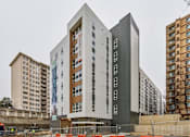 Thumbnail 1 of 17 - A modern building with a mix of white and dark grey panels stands in front of a construction site.