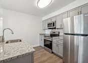 Thumbnail 6 of 22 - A modern kitchen with a stainless steel refrigerator and a granite countertop.