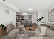 Thumbnail 4 of 22 - A modern living room with a grey couch, a coffee table, and a kitchen in the background.