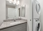 Thumbnail 15 of 22 - A modern bathroom with a granite countertop and a washer and dryer built into the wall.