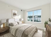 Thumbnail 7 of 22 - A bedroom with a large bed, a nightstand with a lamp, and a window overlooking a building.