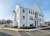 Thumbnail 1 of 22 - A white building with a parking lot in front.
