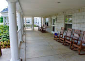 Thumbnail 12 of 13 - A spacious porch with white columns and rocking chairs.