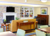 Thumbnail 3 of 21 - A community room with a fireplace, bookshelves, and a painting.