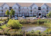 Thumbnail 1 of 8 - A large apartment complex with a pond in front.