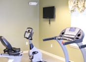 Thumbnail 7 of 8 - A gym with a treadmill and a stationary bike.