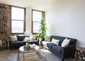 Thumbnail 2 of 9 - A living room with a couch, coffee table, and a plant.